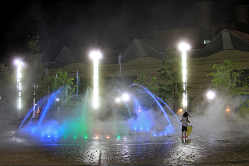 夜の公園で噴水と戯れる少女。